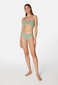 Grön rippad bikini med en bandeau-topp som har en rosettdetalj och matchande låg midja-bakdelar. Materialet verkar texturerat och elastiskt.