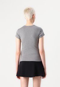 Maglietta grigia a maniche corte, aderente, con scollatura rotonda, realizzata in tessuto morbido, abbinata a una gonna nera fluida. Vista da dietro, design minimalista.