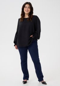 Black long-sleeve blouse with puffy sleeves and a rounded hem, paired with dark blue flared jeans and black pointed-toe flats.