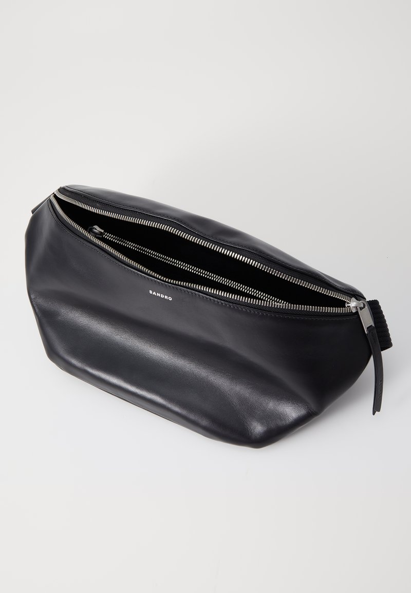 Sac en cuir noir avec une texture lisse, forme ovale, fermeture éclair argentée et logo de marque. Possède un intérieur spacieux et ouvert.