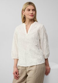Witte geborduurde blouse met een V-hals en driekwart mouwen, met ingewikkelde bloemenpatronen en een lichte, gestructureerde stof.