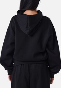 Sudadera negra de gran tamaño con capucha, que presenta puños y dobladillo acanalados. Fabricada en una tela suave con una textura lisa. Vista trasera mostrada.