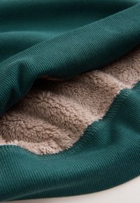 Tissu côtelé bleu sarcelle superposé à une polaire beige douce, mettant en valeur le contraste des textures et des coutures lisses le long des bords.