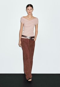 Off-the-shoulder lyserød top med draperet design, parret med brune ruskinds brede bukser og et brunt bælte med en sølvspænde.