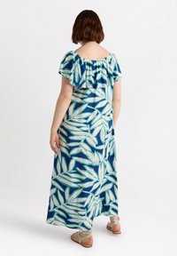 Off-shoulder maxiklänning i blått med vita och gröna bladmönster. Mjuk tyg med volangdetaljer vid ärmarna och en svepande silhuett.