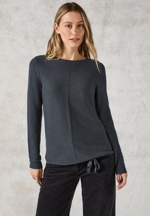 Top long à manches longues en tricot gris foncé avec un col bateau, présentant un tissu texturé et un détail de nœud en bas à droite.