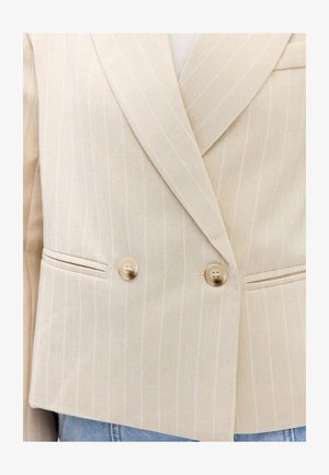 Blazer beige à fines rayures, croisé, à revers crantés, deux boutons et poches passepoilées, porté sur un jean bleu clair.