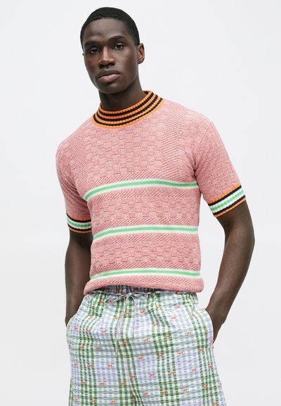 Πλεκτό πουλόβερ με κοντά μανίκια σε ροζ απόχρωση με υφασμάτινο μοτίβο, που διαθέτει πράσινες και μπλε ρίγες στο στήθος και μαύρο και πορτοκαλί ribbed γιακά.