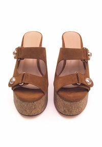 Sandali platform in suede marrone con ampia cinturino e dettagli metallici circolari. Suola in sughero a cuneo, design open toe e fodera morbida.