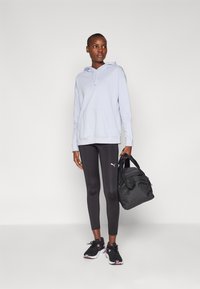 Hanorac albastru deschis cu buzunar frontal, colanți negri și pantofi sport negri. Geantă gri cu două mânere. Design simplu, fără modele.