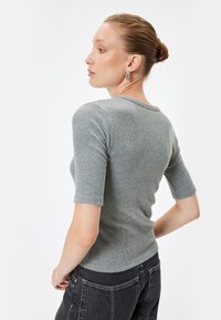 Grijs geribbelde top met korte mouwen en een aansluitend ontwerp en ronde halslijn, gecombineerd met hoge taille donkere jeans, vanuit de achterkant getoond.