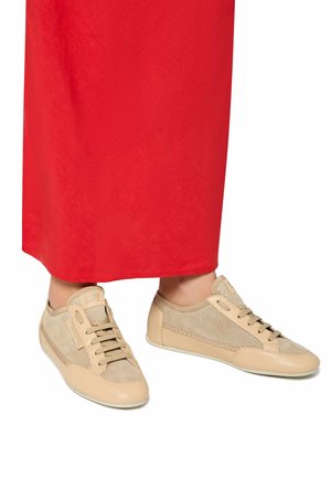 Beige athletic shoes made of perforated material with smooth accents. Features a flexible sole and traditional lacing, paired with a red skirt.