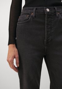 Jean en denim noir avec une taille haute, un design classique à cinq poches, une quincaillerie couleur cuivre et des détails de coutures discrètes.