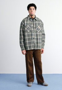 Ternet flannel-skjorte i grønt, marineblåt og beige med to brystlommer. Sammen med brune bukser med vidde og grå sneakers.