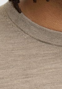 Beige stickad tröja med en texturerad yta och rundad halsringning, med subtila sömnadsdetaljer längs kragen.