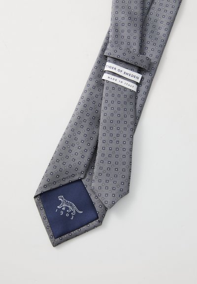 Siva svila kravata s geometrijskim uzorkom, plava podstava s logotipom tigra i oznakom "Tiger of Sweden, Made in Italy."