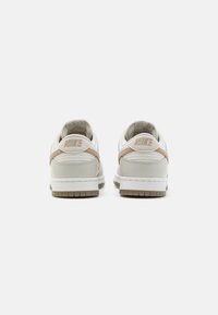 Tenisky Nike Dunk Low v světle krémové barvě s béžovými detaily. Mají hladký kožený svršek a texturovanou gumovou podrážku. Na zadní straně je logo.