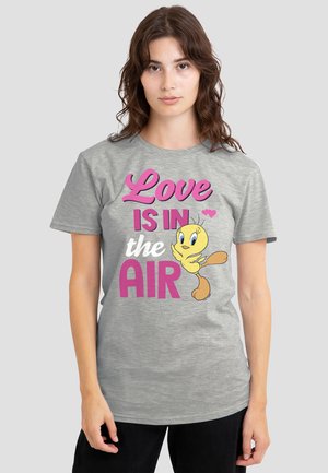 Woman wearing a gray t-shirt with pink and white text "Love is in the air" and a yellow Tweety Bird cartoon character.