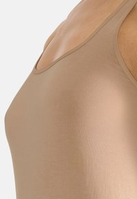Nude linne med ett mjukt, stretchigt tyg. Har tunna axelband och en rundad halsringning. Lätt, mjuk textur med en åtsittande design.