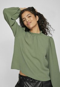 Groene, gestructureerde blouse met lange mouwen, een ruffled halslijn en ballonmouwen, gecombineerd met een zwarte tailleband met hoge taille.