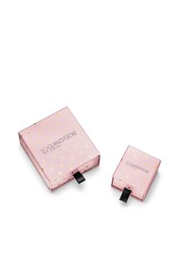 Rozā dāvanu kārbas, viena lielāka, otra mazāka, ar zelta sirdspatērēm, melnu vilkšanas cilpu un uzrakstu "GLANZSTÜCKE MÜNCHEN" sānos.