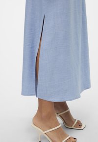 Ljusblå maxiklänning med sidslitsar, tillverkad av ett mjukt, texturerat tyg. Kombinerad med beiga, remmade högklackade sandaler.