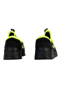 Zapatillas deportivas negras con acentos en amarillo neón, parte superior de malla texturizada y suelas gruesas de goma negra; cuenta con tiradores en la parte trasera.