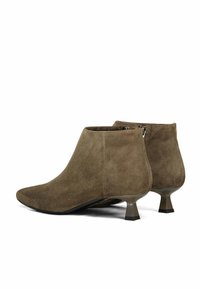Bottines en cuir suede marron avec un bout pointu et un talon bas carré. Elles présentent une texture lisse et un détail de fermeture éclair à l'arrière.