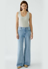 Light blue wide-leg jeans with a high waist, styled with a fitted gray tank top. Smooth texture, reinforced stitching, and front pockets.