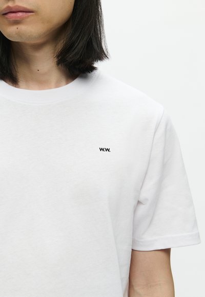Λευκό βαμβακερό t-shirt με στρογγυλή λαιμόκοψη και κοντά μανίκια. Φέρει ένα μικρό μαύρο λογότυπο "W.W." στο στήθος. Λείο ύφασμα.
