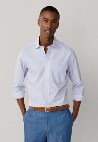 Chemise pour homme à boutons en bleu clair avec fines rayures blanches, dotée d'une poche poitrine et de manches retroussées, assortie à un pantalon bleu clair.
