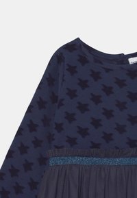 Vestido azul marinho com padrão de estrelas, mangas longas e uma cintura texturizada com um acabamento brilhante. Tecido suave com saias em forma de flared.