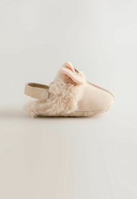 Chaussure bébé beige douce avec bordure en fausse fourrure, un nœud en tissu et une lanière arrière, vue de profil sur un fond neutre.