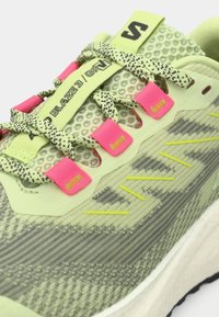 Πράσινο αθλητικό παπούτσι με υφή στην επάνω επιφάνεια, με ροζ και μαύρες λεπτομέρειες, πάνελ από δίχτυ και παχύ λευκό ενδιάμεσο σόλα. Τα κορδόνια έχουν σχέδιο.
