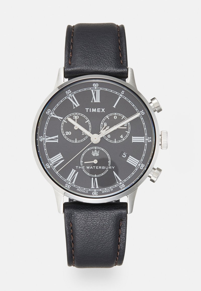 Montre avec un bracelet en cuir noir et un boîtier en acier inoxydable argenté. Le cadran noir présente des chiffres romains en argent, des sous-cadrans et un affichage de la date.