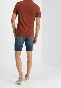 Hnědé polo tričko s krátkým rukávem, zkombinované s modrými denimovými šortkami a šedými teniskami. Šortky mají roztrhaný lem a design s pěti kapsami.