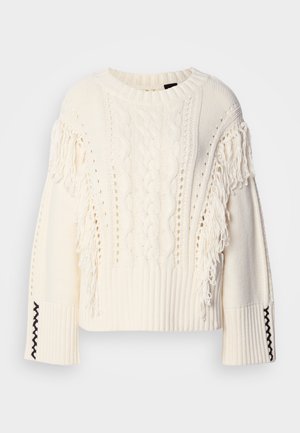 Pull en tricot couleur crème avec des motifs en cable, des détails en franges sur les manches et des poignets côtelés avec des coutures accentuées en noir.