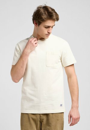 T-shirt crema a maniche corte con taschino sul petto, realizzato in cotone morbido, con colletto rotondo e un'etichetta discreta del marchio sull'orlo.