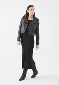 Chaqueta de motociclista de cuero negro sobre un vestido maxi de canalé negro, combinado con botas vaqueras negras con detalles en relieve.