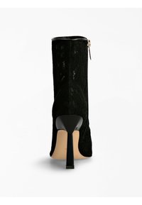 Stivaletto alla caviglia in pizzo nero con tacco alto e lucido di colore nero. Presenta una chiusura con zip sul lato e un tessuto in pizzo decorato con una fodera liscia.