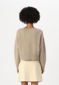 Maglione beige lavorato a maglia con vestibilità morbida, texture a coste e orlo cropped, abbinato a una gonna di colore chiaro con tasche posteriori.