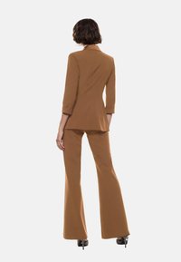 Blazer marrone su misura e pantaloni svasati realizzati in un tessuto liscio. Maniche lunghe arrotolate ai polsi, con un design di revers classico.