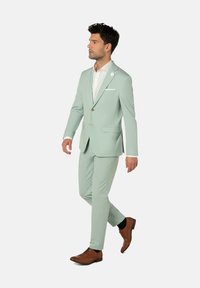 Helles grünes Suit aus glattem Stoff, mit Revers, weißem Hemd und braunen Leder-Schuhen. Enthält eine Einstecktuch und eine Nadelapplikation.