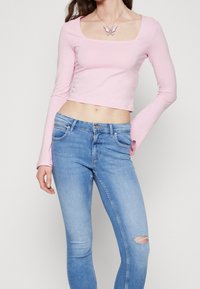 Top corto rosa de mangas largas con escote cuadrado, combinado con jeans ajustados de un azul claro con un detalle de rodilla desgastada.