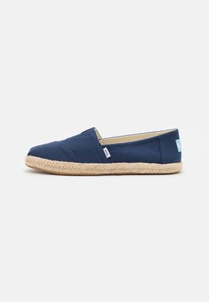 Marineblauwe canvas instapschoen met beige gevlochten jutenzool en een klein zijlabel tegen een effen achtergrond.