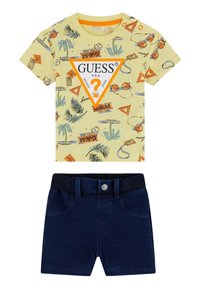 T-shirt graphique jaune avec imprimés de palmier et de basket-ball, associé à un short en denim bleu marine avec une taille élastique et un bouton.