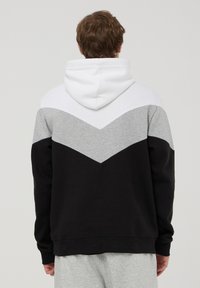 Felpa con cappuccio in nero, grigio e bianco. Presenta un design a chevron sulle spalle. Materiale in misto cotone con polsini e orlo a coste.