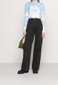 Blusa de manga larga con patrones abstractos en azul y blanco, combinada con unos vaqueros anchos de talle alto en negro y un pequeño bolso verde oliva. Botas de plataforma negras.
