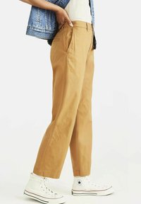 Khaki vida byxor med en mjuk textur, med sidofickor och sydda sömmar, i kombination med vita högskurna sneakers.