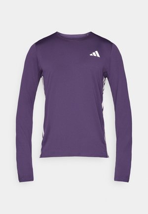Camiseta deportiva de manga larga en color púrpura, con cuello redondo, tejido texturizado y detalles de logo blanco en la parte superior izquierda del pecho y los lados.
